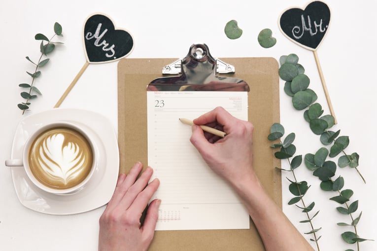 Woman Writing On Wedding Calendar. Flat Lay Composition With Coffee And Decorations. Wedding Planner